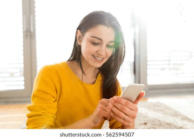 Woman At Home Sitting On Carpet, Holding Smart Phone, Texting