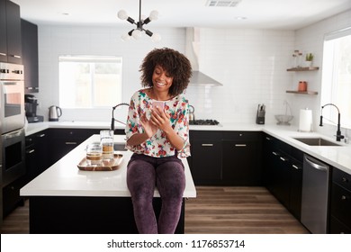 Woman At Home Sitting On Kitchen Island Whilst Using Mobile Phone - Powered by Shutterstock