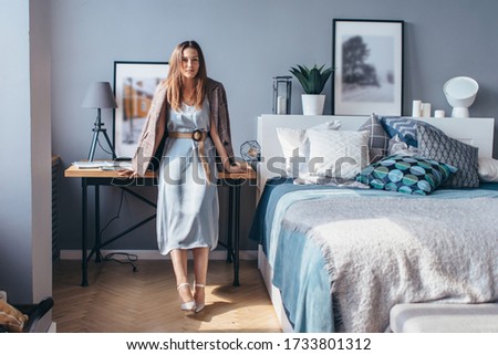Woman at home stands in bedroom at bedside table.