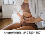 Woman at home suffering from menstrual pain, having cramps. Close up of woman holding abdomen, endometriosis, and conditions causing pain in tummy.