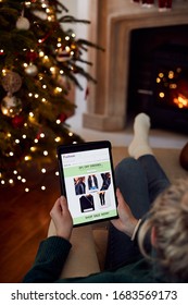 Woman At Home Using Digital Tablet To Shop For Clothes Online At Christmas