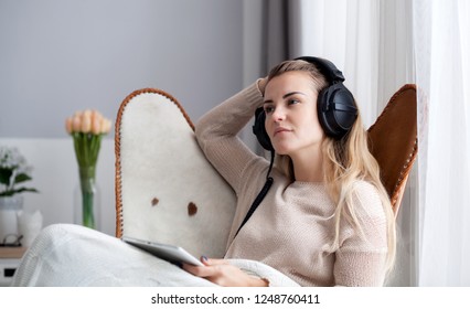 Woman at home wearing headphones while using digital tablet, listening to audiobooks or music