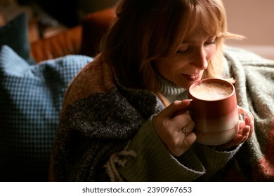Woman At Home Wearing Winter Jumper And Blanket With Warming Hot Drink Of Coffee In Cup Or Mug