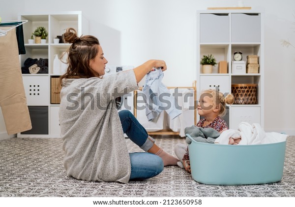 A woman in\
homespun clothes sits on the bathroom floor by a bowl of colorful\
laundry she is sorting, next to her mother sits a little girl with\
blonde hair tied in two buns
