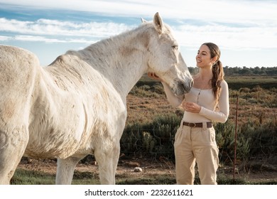 Woman with horse feeling freedom relaxed in the field outdoors at sunset with golden sunlight. True friendship. Girl taking care of her white horse on the meadow. Equestrian Physiotherapy. - Powered by Shutterstock