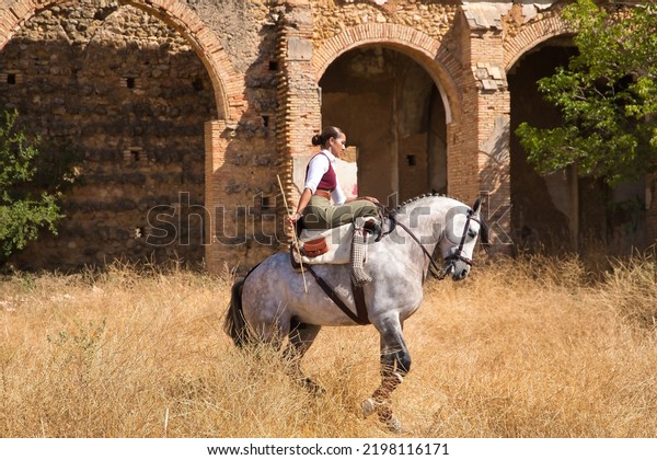 Woman horsewoman, young and beautiful,\
performing cowgirl dressage exercises with her horse, in the\
countryside next to a ruined building. Concept horse riding,\
animals, dressage, horsewoman,\
cowgirl.