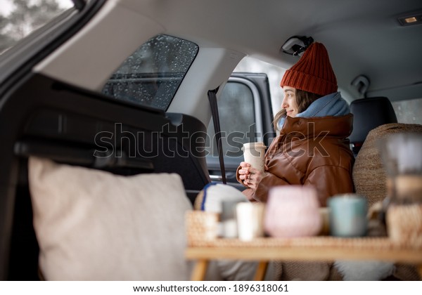 Woman with hot drink sitting in car and have a\
picnic, look at the forest, traveling by car during winter\
holidays. High quality\
photo
