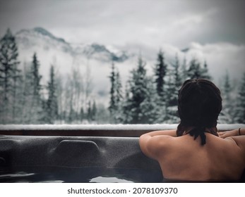Woman in hot tub in winter looking at mountain view