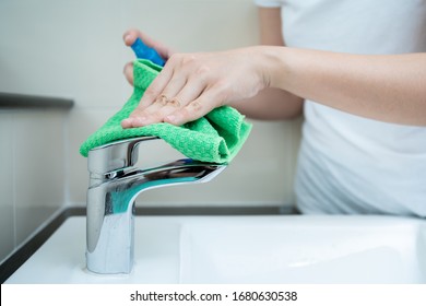 Woman House Keeper Cleaning A Dirty Stainless Water Tap On The Wash Basin In Toilet. Maid Spraying Liquid Cleaning Solution On The Dirty Faucet In Toilet And Using Micro Fabric Wipe On A Water Tab.