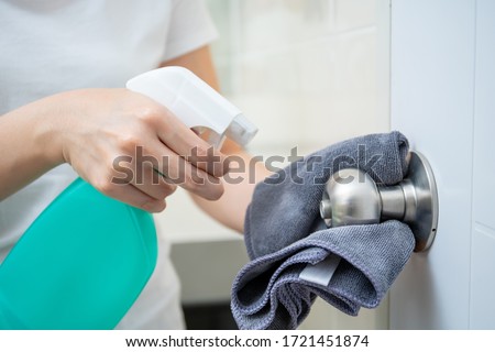 Woman house keeper cleaning a dirty stainless door knob in toilet. Maid spraying liquid cleaning solution on the dirty door knob handle in toilet and using micro fabric wipe on door knob surface.