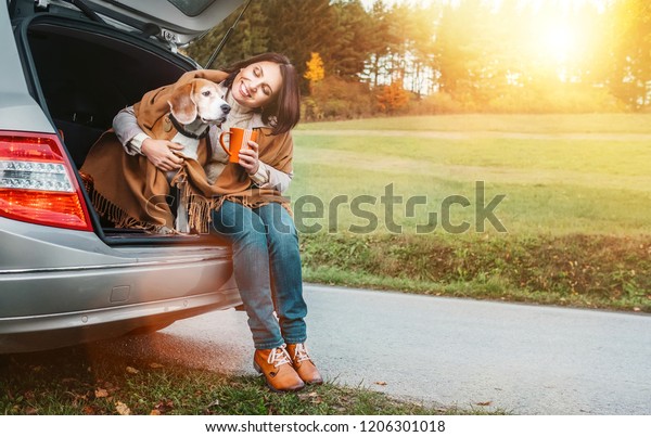 Woman huges her dog with shawls sitting together in\
car trunk