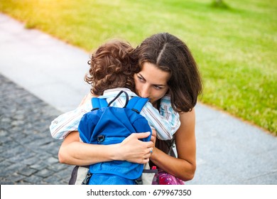 A Woman Hugs A Curly-haired Boy And Smiles. Mom Feels Sorry For Her Son. Meeting Mom And Baby After Separation. A Child With A Backpack Hugs Her Mother.