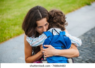 A Woman Hugs A Curly-haired Boy And Smiles. Mom Feels Sorry For Her Son. Meeting Mom And Baby After Separation. A Child With A Backpack Hugs Her Mother.