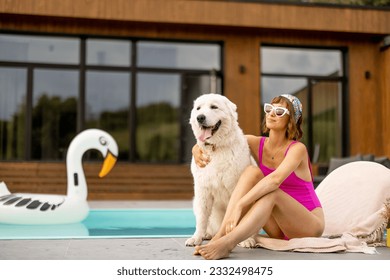 Woman hugs with her cute white dog while relaxing near house with a swimming pool. Friendship with pets and summer vacation concept - Powered by Shutterstock