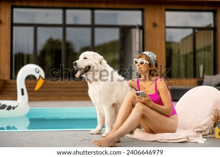 Woman hugs with her cute white dog while relaxing near house with a swimming pool. Friendship with pets and summer vacation concept