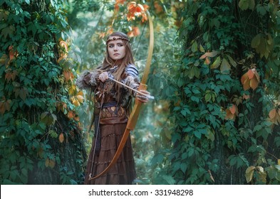 Woman Hunter With A Bow In Hand, Taking Aim At His Prey In The Forest. Amazon
