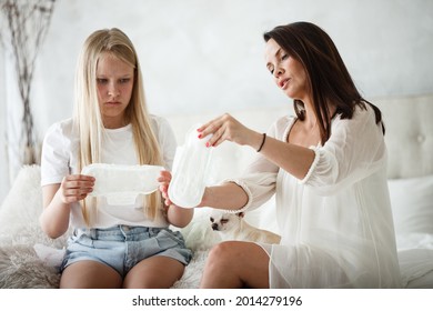 Woman hygene concept. Periods. Menstrual cycle. Mother explains daughter how to use hygiene pads and tampons. Woman and teenage girl talking at home.