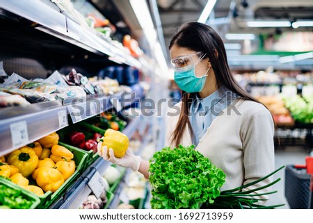 Woman with hygienic mask buying in supermarket grocery store for fresh greens,shopping during the pandemic.Natural source of vitamins and minerals.Plant based diet.Covid-19 quarantine preparation