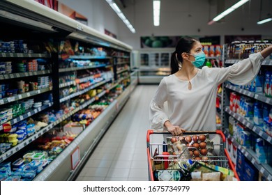 Woman With Hygienic Mask Shopping For Supply.Budget Buying At A Supply Store.Emergency To Buy List.Shopping For Enough Food And Cleaning Products.Preparation For A Pandemic Quarantine Due To Covid-19