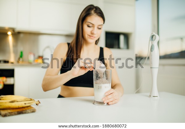 Woman with immersion blender making banana\
chocolate protein powder milkshake smoothie.Adding a scoop of low\
carb whey protein mix to shake after a home workout.Diet after the\
gym.Healthy lifestyle