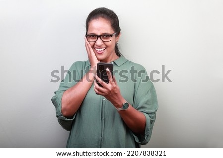 Woman of Indian ethnicity with a smiling face holding a mobile phone 
