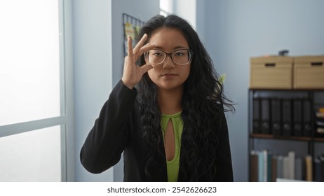 Woman indoors adjusting glasses in modern office setting, showing confident demeanor with long black hair and wearing a green top and black jacket. - Powered by Shutterstock