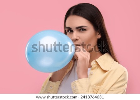 Woman inflating light blue balloon on pink background