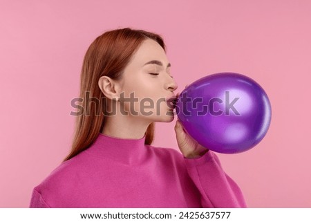 Woman inflating purple balloon on pink background