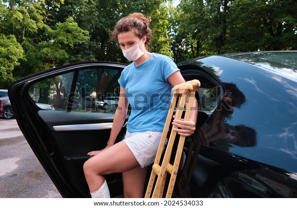 A woman with an\
injured leg gets into a car. Orthopedic plaster, orthopedic\
crutches. Limited mobility