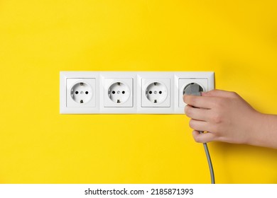 Woman inserting plug into power socket on yellow wall, closeup. Electrical supply - Shutterstock ID 2185871393