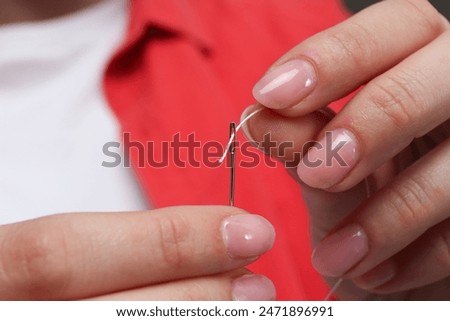 Woman inserting thread through eye of needle, closeup