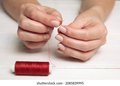 A woman inserts a red thread into a needle. Hands close-up.
