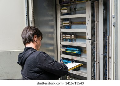 A woman inspects the electrical cabinet of a machine and takes notes. - Shutterstock ID 1416713543