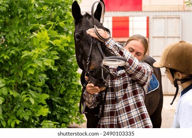 Woman instructor adjusting bridle on horse while interacting with young rider girl. Horse riding activity - Powered by Shutterstock