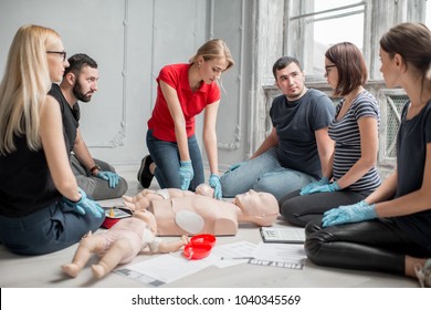 Woman instructor showing how to make chest compressions on a baby dummy during the first aid group training indoors - Powered by Shutterstock