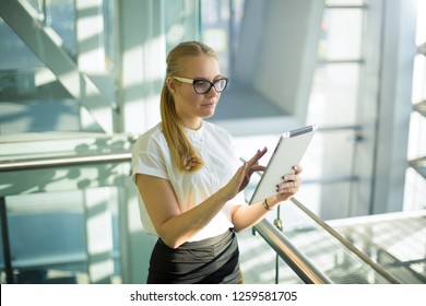 Woman intelligent government worker using applications via touch pad while standing in modern office interior.Female proud candidate searching information via digital gadget standing inside enterprise