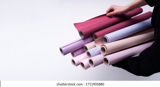 Woman Interior Designer Holding In Hands Scrolls Of Paper Rolls. Rolls Of Pastel Colors Wallpapers On White Background. Copy Space For Text. Construction Materials Delivery And Selection Assistance