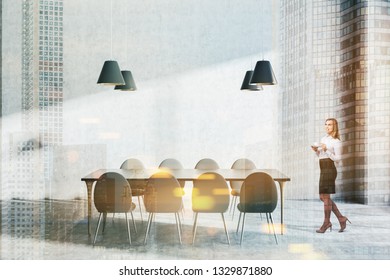 Woman in interior of minimalistic dining room with concrete walls and floor, long gray table soft with gray chairs and four stylish ceiling lamps. Toned image double exposure