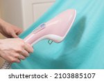 Woman ironing green shirt handheld garment steamer. Vertical steam irons brushes for ironing clothes generator. Household garment steamer handheld ironing machine