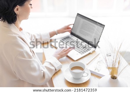Woman in a jacket is typing in a text document on her laptop. Sitting at the desk with a cup of coffee. Close-up of eyelashes.
