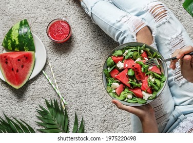 Woman In Jeans Eating Fresh Summer Watermelon Salad With Feta Cheese With Smoothie On Light Background With Tropical Leaves. Healthy Food, Clean Eating, Buddha Bowl Salad, Top View