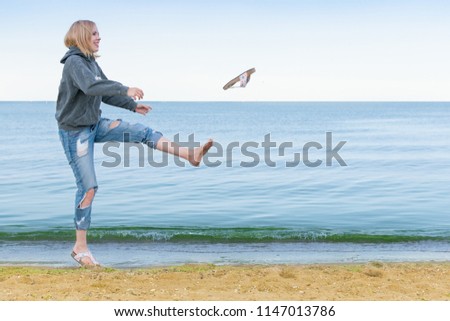 A woman in jeans jumps happily on the beach. The shoes go off their feet.