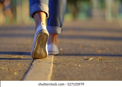 Woman jeans and sneaker shoes walking on the road sunset light