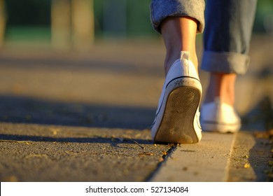 Woman jeans and sneaker shoes walking on the road sunset light