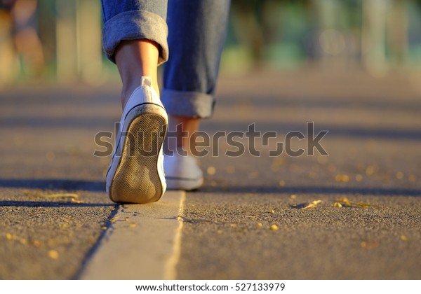 道路の夕日の光の中を歩く女性のジーンズとスニーカーの靴 の写真素材 今すぐ編集