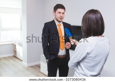 A woman journalist interviews a business man in a suit in a room with a modern interior