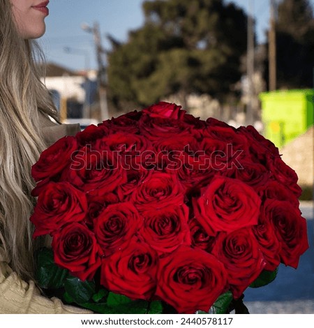 A woman joyfully holds a stunning bouquet of vibrant red roses, providing a beautiful focal point with ample copy space.