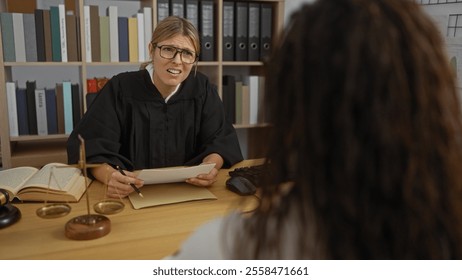 Woman judge talking to client indoors in courthouse office with legal books and scales on desk. - Powered by Shutterstock