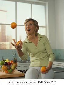 Woman Juggling Oranges In Kitchen