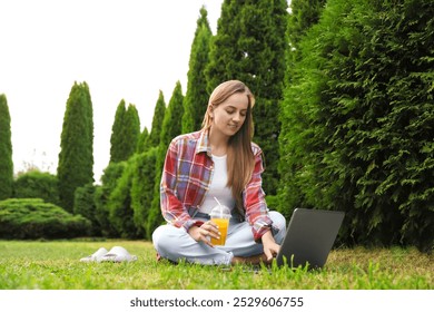 Woman with juice using laptop on green lawn in park - Powered by Shutterstock